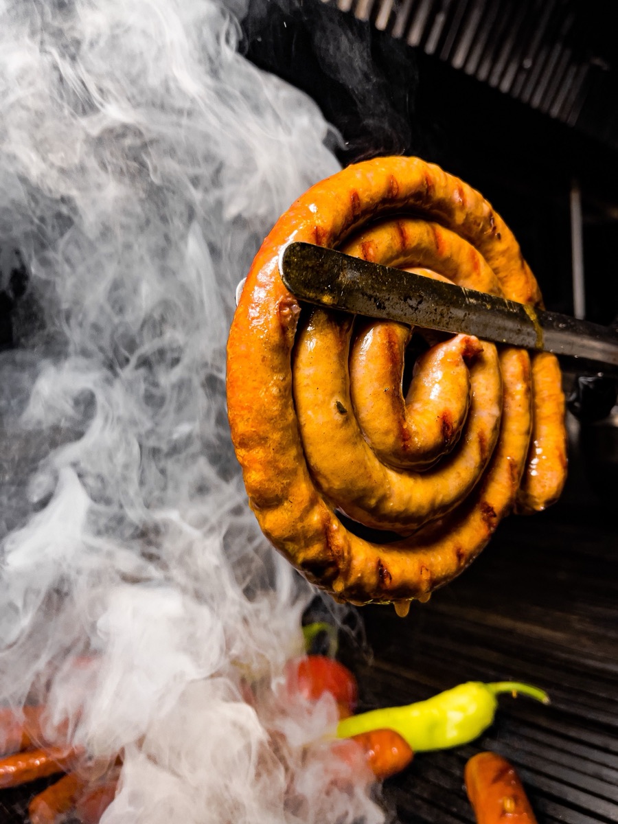 A coiled sausage in natural casing lifted from a smoking grill