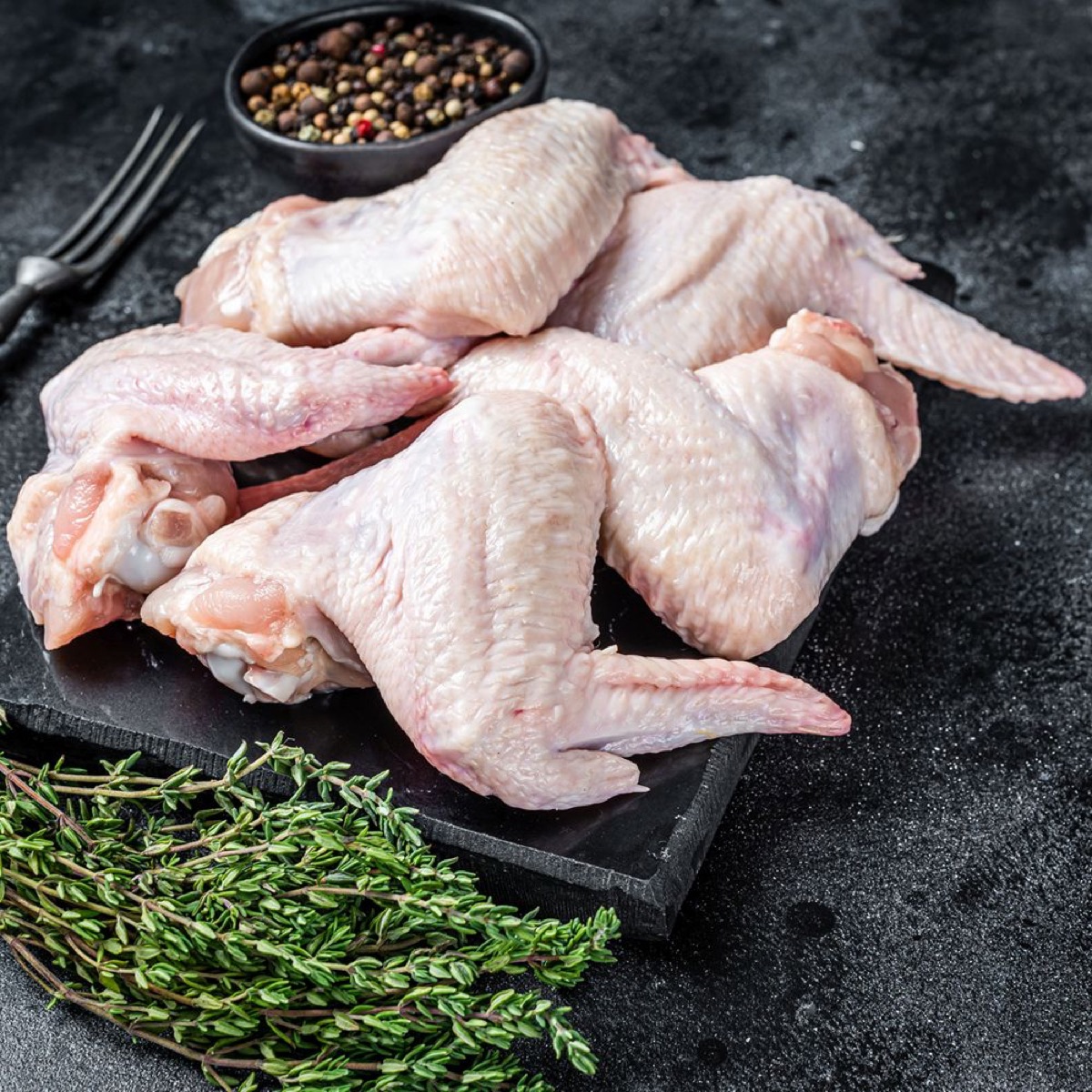 Fresh chicken wings arranged on a dark slate board with thyme