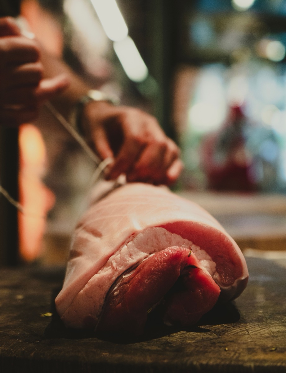 A pork loin being trimmed by hand under warm light