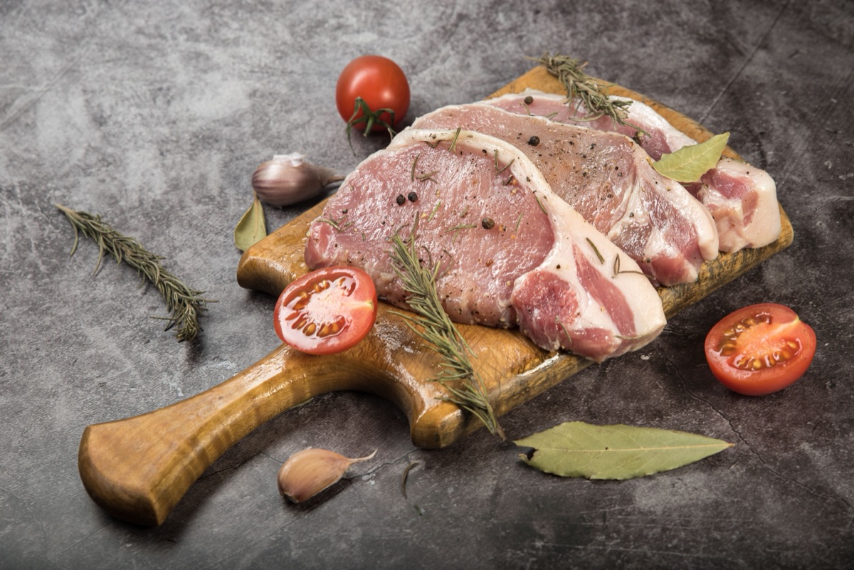 Trimmed pork loin on a wooden board with rosemary and tomatoes